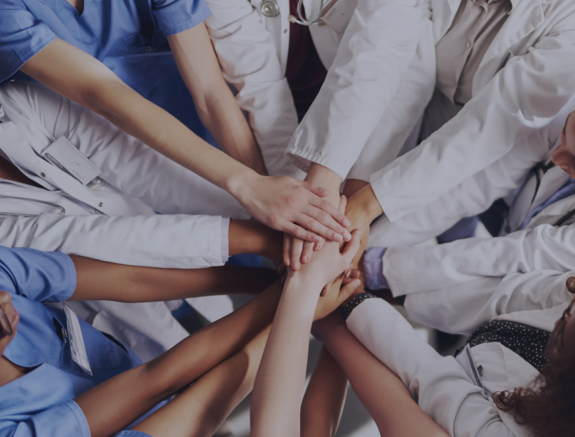 Healthcare professionals stack hands in unity, symbolizing collaboration, diversity, and collective impact in healthcare.