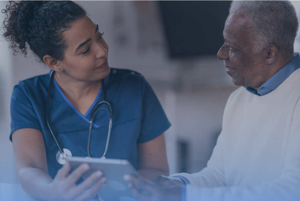 A healthcare professional in scrubs holding a tablet speaks compassionately with an older patient, symbolizing patient-provider trust and shared decision-making.