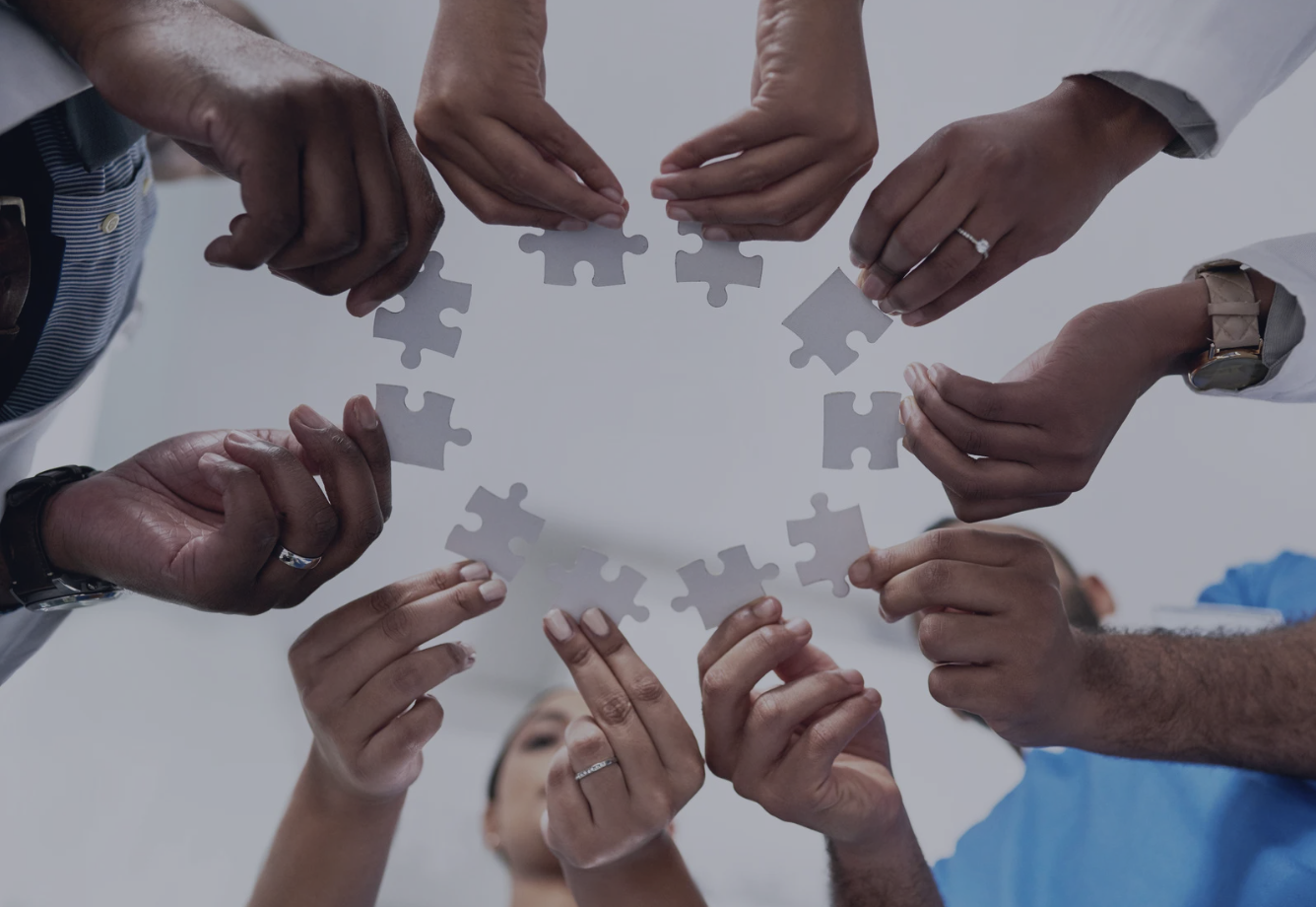A group of diverse hands holding puzzle pieces in a circle, symbolizing collaboration, integration, and equity in healthcare.