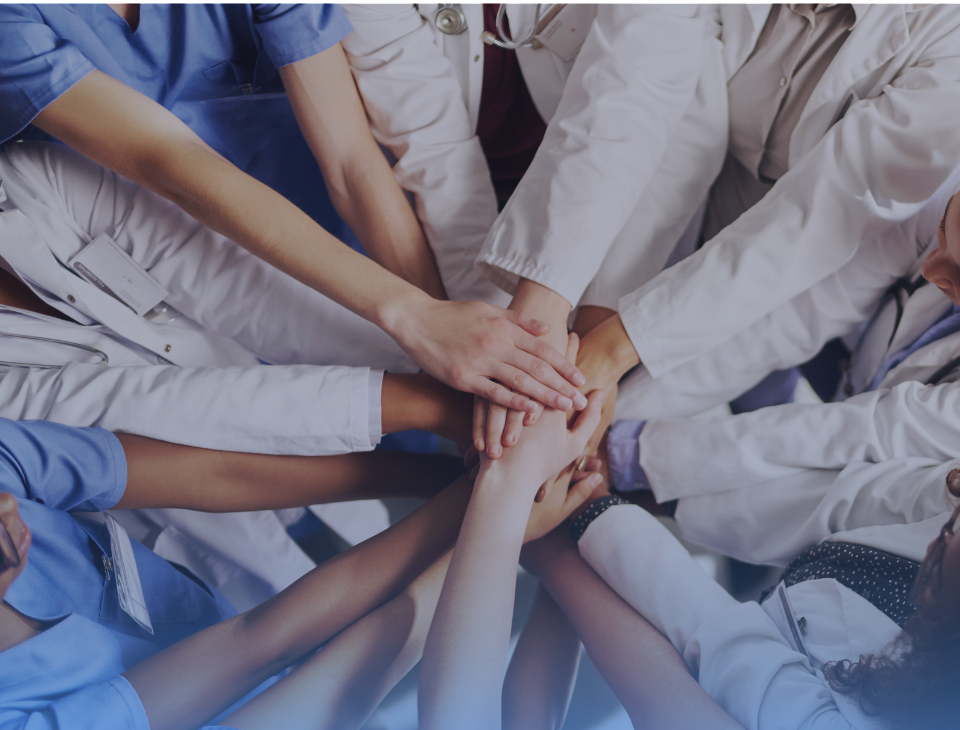 Healthcare professionals stack hands in unity, symbolizing collaboration, diversity, and collective impact in healthcare.